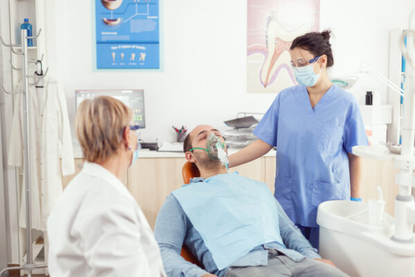 Orthodontist assistant putting oxigen mask to patient analyzing teeth pain during stomatology appointment. Medical team working in dentistry clinic office checking tooth preparing for surgery